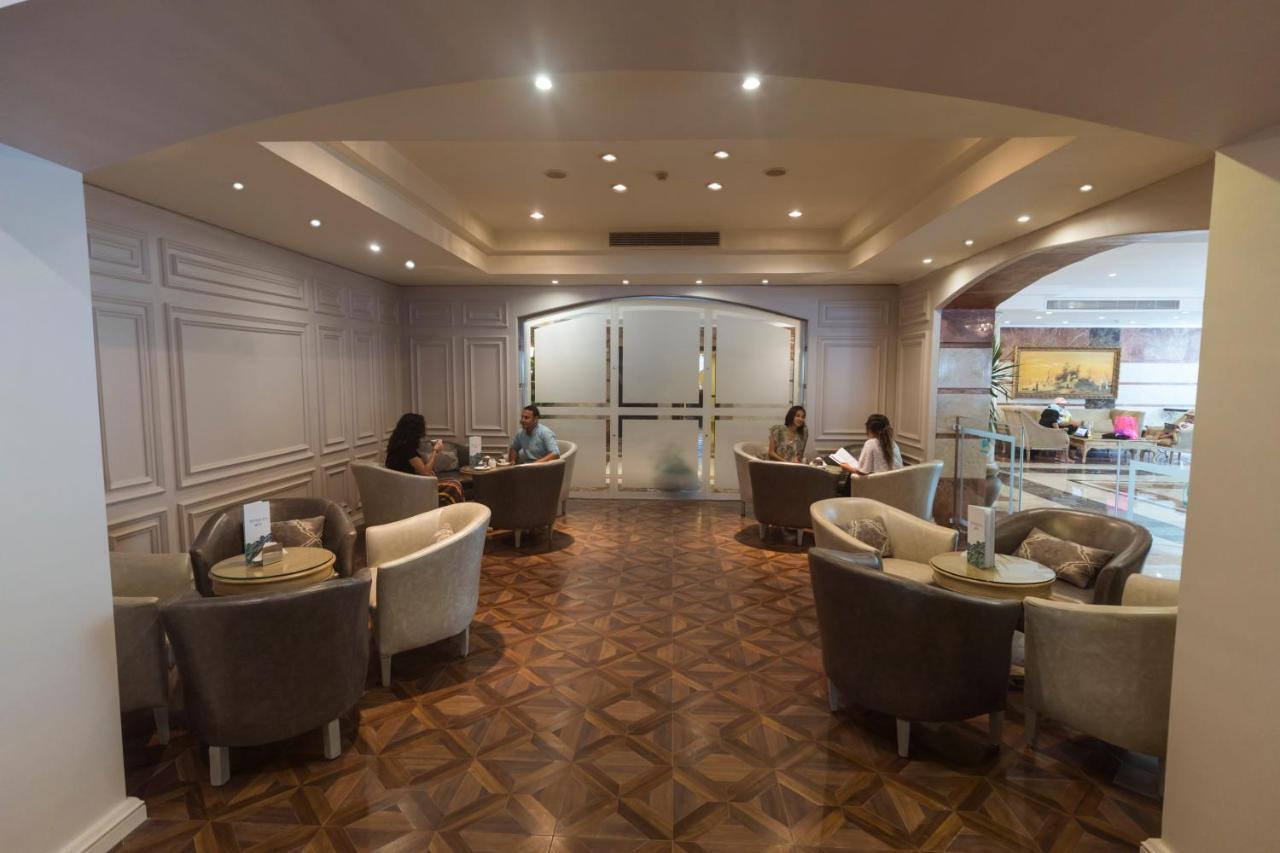 Sunrise Alex Avenue Hotel Aleksandria Zewnętrze zdjęcie The photo shows a well-lit lounge area with a modern and elegant design. There are several comfortable seating arrangements, including plush chairs and small tables. The flooring appears to be made of a decorative wood pattern. In the background, the