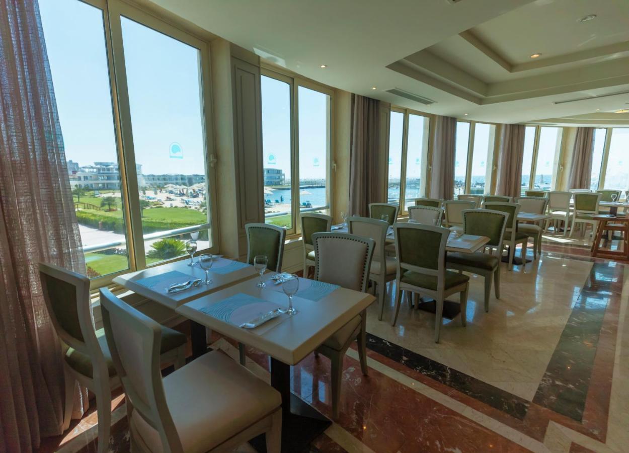 Sunrise Alex Avenue Hotel Aleksandria Zewnętrze zdjęcie The photo shows an elegant restaurant interior with several tables and chairs arranged in a spacious setting. The dining area features large windows that allow natural light to flood in, offering a view of the outdoor landscape. The tables are set wi