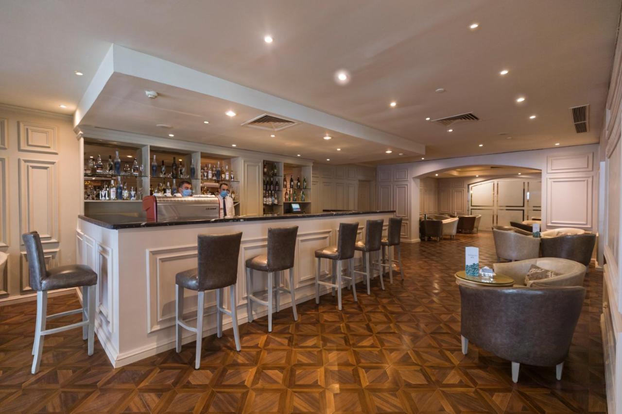 Sunrise Alex Avenue Hotel Aleksandria Zewnętrze zdjęcie The photo shows a modern bar area with a sleek, minimalist design. The bar itself features a long countertop with several high-backed chairs positioned in front of it. Behind the bar, shelves are lined with various bottles of alcoholic beverages. The
