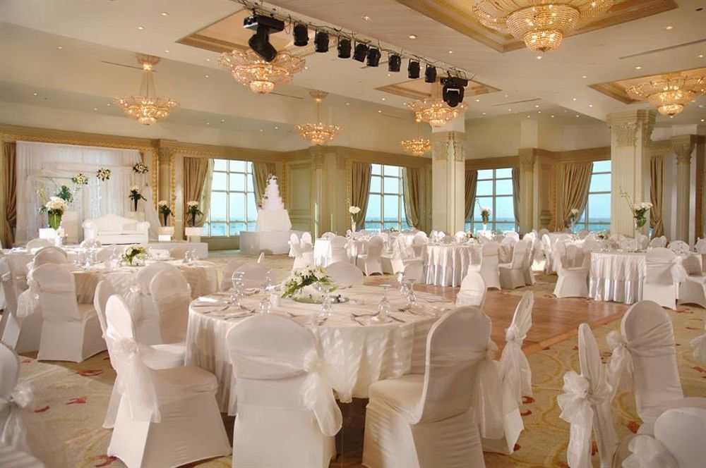 Sunrise Alex Avenue Hotel Aleksandria Zewnętrze zdjęcie The photo depicts an elegant banquet hall set up for a formal event, likely a wedding or reception. The room features several round tables covered with white tablecloths and adorned with floral centerpieces. Chairs are also dressed in white covers, c