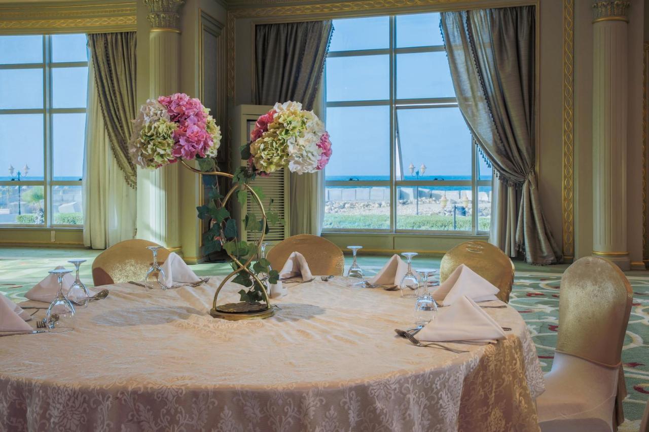 Sunrise Alex Avenue Hotel Aleksandria Zewnętrze zdjęcie The photo depicts a beautifully arranged round dining table set in an elegant room. The table is covered with a light-colored lace tablecloth and features an artistic floral centerpiece with pink and white flowers. The place settings include folded n